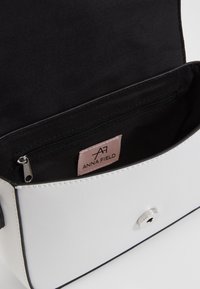 Vitt läderhandväska med svarta detaljer, med ett zip-inre fack och ett silverfärgat tryckknappsstängning. Märkesetikett synlig inuti.