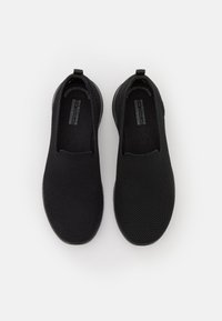 Chaussures noires à enfiler en mesh respirant avec un dessus texturé, un bout rond et une semelle en caoutchouc. Comprend une languette au talon.