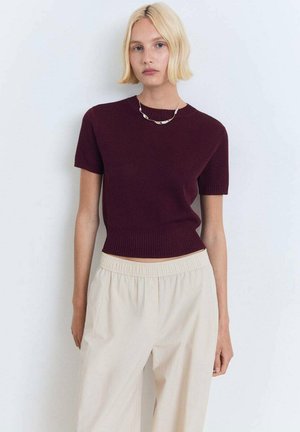 Maroon knitted short-sleeve top with a ribbed neckline and hem, paired with light beige loose trousers. Smooth texture and fitted silhouette.