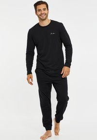 Sort langærmet crew neck bluse med broderet logo, parret med matchende sorte joggerbukser med ribbede manchetter og sidelommer.