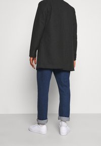 Blazer grigio scuro con due bottoni, abbinato a jeans in denim blu scuro risvoltati e sneakers bianche. Design minimalista, vestibilità sartoriale.