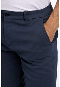 Mörkblå bomullsbyxor med slim fit, med knappstängning, sidofickor och synliga sömnadsdetaljer. Slät yta.