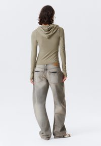 Long-sleeve olive green hoodie with a fitted design, paired with light gray wide-leg jeans featuring a faded texture and back pockets.