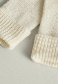 Krém színű kötött pulóver mandzsetták, lágy, bolyhos textúrával. A szélén bordázott mintázat rugalmas illeszkedést biztosít.