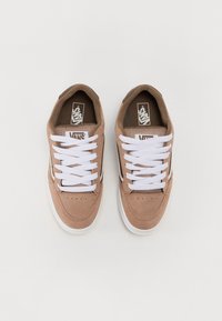 Hnědé semišové tenisky s bílými tkaničkami, gumovou podrážkou a síťovinovými detaily. Na jazyku a bočním pruhu se nachází podpisové logo.