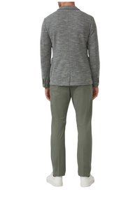 Grijze gestructureerde blazer met een enkele split, gecombineerd met lichtgroene broek en witte sneakers, gezien vanuit de achterkant.