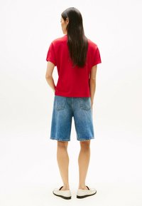 T-shirt rosso a maniche corte, pantaloni corti in denim blu e scarpe slip-on beige. La t-shirt ha una vestibilità comoda; i pantaloni corti arrivano sopra il ginocchio. Texture morbide.