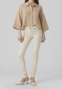 Beige texturovaná košile s knoflíky a širokými rukávy, kombinovaná s lehkými krémovými skinny džíny a světlými béžovými nazouvacími mules.