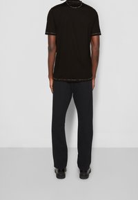 Svart kortärmad T-shirt med flerfärgad kant på kragen och ärmsluten, parat med svarta sweatpants och svarta skor, sett bakifrån.