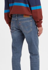 Vaqueros de mezclilla azul claro con un diseño ajustado, costura reforzada, dos bolsillos traseros y una etiqueta de cuero marrón en la cinturilla.