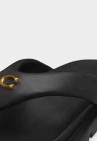 Μαύρο σανδάλι με μαξιλαράκι και φαρδιά λουρί που διαθέτει μικρή χρυσή αγκράφα σε σχήμα πετάλου.