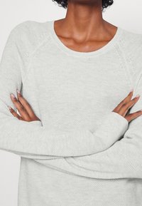 Helles grauer Strickpullover mit rundem Halsausschnitt, gerippten Bündchen und strukturiertem Muster. Verfügt über lange Ärmel und eine lockere Passform.