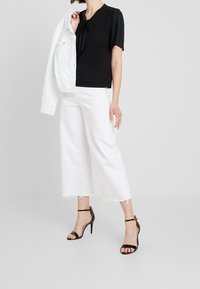 Svart kortärmad blus med rosett, kombinerad med vita korta jeans med fransiga fållar och svarta högklackade sandaler med remmar.