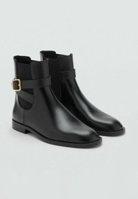Botine din piele neagră până la gleznă, cu o finisare netedă, panouri laterale elastice și un accent cu cataramă aurie pe curea. Talpă plată.