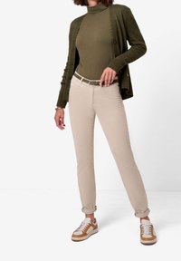 Beige slim-fit byxor kombinerat med en mörkgrön ribbad cardigan och en grön polotröja. Vita och bruna sneakers fulländar outfiten.