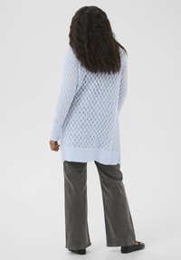 Hellblauer Strickpullover mit einem Rautenmuster, langen Ärmeln und geripptem Saum, kombiniert mit grauen weit geschnittenen Hosen.