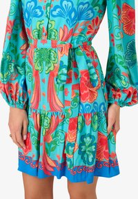 Vestito floreale colorato con una base blu vivace, maniche a sbuffo, vita con fiocco e orlo a strati con intricati motivi in rosso e verde.
