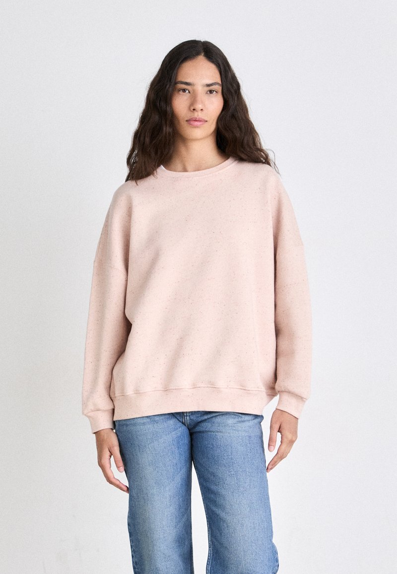 Lichtroze sweatshirt van zacht materiaal, met een ronde halslijn, ingezette schouders en geribbelde manchetten, gestyled met blauwe jeans.