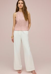 Top roz deschis fără mâneci, cu dungi texturate, asortat cu pantaloni albi cu picioare largi. Outfitul include sandale roz deschis cu barete.