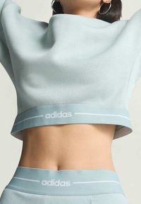 Svetlomodrý skrátený sveter s širokým výstrihom a jemnou textúrou, s bielym logom "adidas" na leme.