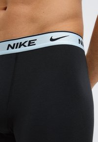 Fekete sport rövidnadrág puha anyagból, világoskék rugalmas derékpánttal, fekete "Nike" márkajelzéssel és varrási részlettel.