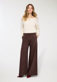 Pantaloni marroni ampi con una finitura strutturata, abbinati a un top crema a maniche lunghe e vestibilità larga. Entrambi i capi presentano dettagli di design minimalisti.