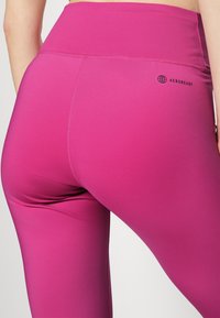 Dopasowane różowe legginsy wykonane z elastycznego materiału, z wysokim stanem i małym czarnym logo "AEROREADY" na plecach.