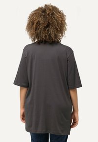 Graues Baumwoll-Übergrößen-T-Shirt mit kurzen Ärmeln, rundem Ausschnitt und seitlichen Schlitzen, getragen mit blauen Jeans. Weicher Stoff, lässiges Design.