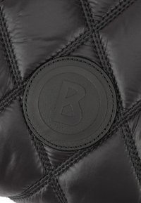 Zwart doorgestikt pufferstof met een ronde zwarte leren logo, met een verhoogde "B" in het midden. Zichtbare zwarte stiknaden als accent.