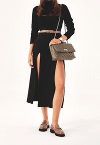 Maglietta nera a maniche lunghe abbinata a una gonna nera con spacchi alti, cintura beige, mocassini marrone chiaro e borsa grigia trapuntata con tracolla a catena.