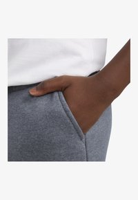 Pantalones de chándal grises con una textura suave, que cuentan con bolsillos laterales y un diseño ajustado, combinados con una camiseta blanca lisa a la altura de la cintura.
