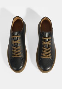 Baskets en cuir noir avec une finition texturée, dotées de lacets beiges et d'une semelle en gomme. Design classique à bout arrondi.