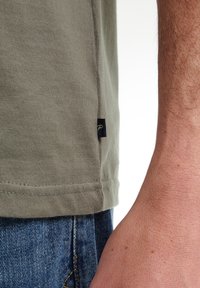 Olijfgroene katoenen T-shirt met een zijnaadlabel, voorzien van een rechte zoom en een zachte textuur, gecombineerd met blauwe denim jeans.