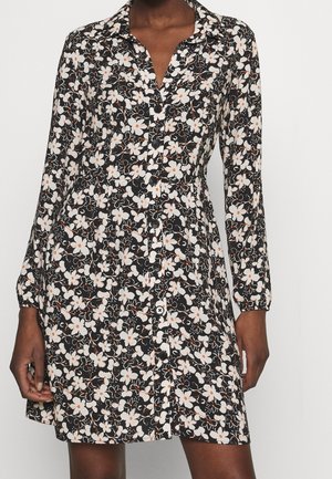 Zwarte jurk met knopen en lange mouwen, met een wit-oranje bloemenpatroon, gedragen door een persoon met een medium-lichte huidtoon.