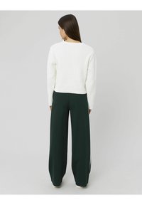 Pull en maille blanche et épaisse avec une texture côtelée et un col rond, associé à un pantalon large vert foncé avec des rayures sur les côtés.