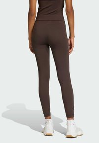 Hnědé legíny vyrobené z elastického materiálu s vysokým pasem, zužujícími se nohavicemi a hladkým povrchem, doplněné bílými sportovními botami.