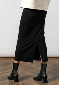 Sort blyantnederdel med en slids bagpå, lavet af strækbart stof. Stylet med sorte ankelstøvler med lynlås og blokhæl.