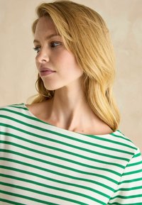 Zaļi un balti svītrainā blūze ar kuģa kakla izgriezumu. Izgatavota no mīksta auduma, ar īsām piedurknēm un brīvu piegriezumu ar horizontālām svītrām.