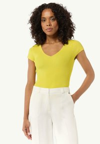 Żółty, prążkowany bodysuit z krótkim rękawem i dekoltem w kształcie V, w zestawieniu z białymi, lnianymi spodniami o wysokim stanie. Widoczne detale struktury i dopasowania.