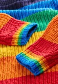Maglioni lavorati a maglia con vivaci righe orizzontali in rosso, arancione, giallo, verde, blu e viola. Texture a costine, materiali in filato morbido.