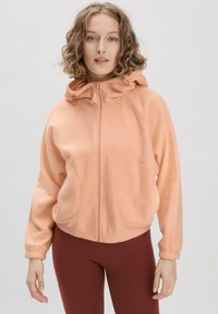 Pfirsichfarbener Fleece-Zipper-Hoodie mit Kapuze und Kordelzug, gro�ßen Fronttaschen und gerippten Bündchen, kombiniert mit figurschmeichelnden burgunderfarbenen Leggings.