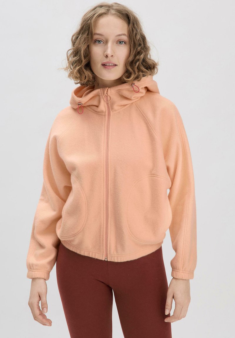 Pfirsichfarbener Fleece-Zipper-Hoodie mit Kapuze und Kordelzug, großen Fronttaschen und gerippten Bündchen, kombiniert mit figurschmeichelnden burgunderfarbenen Leggings.