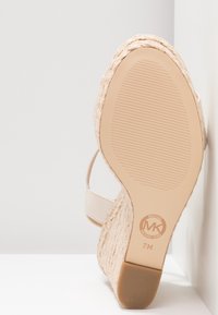 Sandalo con zeppa beige in juta intrecciata, parte superiore liscia, cinturino alla caviglia e suola in gomma con scanalature per la presa. Contrassegnato con il logo MK.