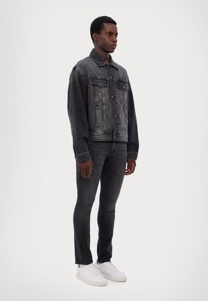 Sort denimjakke med knaplukning, to forlommer og en let falmet overflade, parret med mørke jeans og hvide sneakers.