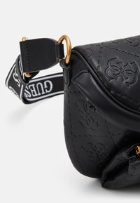 Černá crossbody taška s embosovaným vzorem, s akcentem zlaté kovové části a odnímatelným popruhem s kontrastním logem.