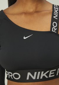 Svart Nike treningssinglet med en skulderdesign, med en hvit Nike-logo og et bredt, teksturert svart bånd med "PRO" i reflekterende sølvbokstaver.