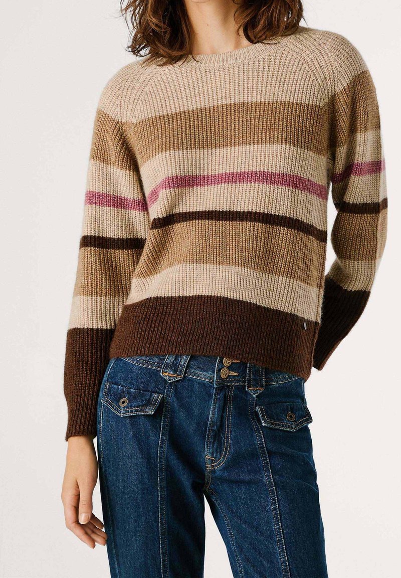 Personne portant un pull en maille côtelée avec des rayures horizontales marron, beige et rose, associé à un jean en denim bleu avec des poches à rabat boutonnées.