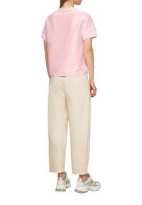 Rosa-weißer gestreifter Kurzarm-Top kombiniert mit crèmefarbenen weit geschnittenen Hosen und grauen Sportschuhen. Die Rückansicht zeigt die entspannte Passform und die Länge.