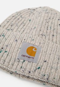 Gorro de punto en gris claro con textura acanalada, que presenta motas multicolores y una etiqueta rectangular gris con un logo naranja.