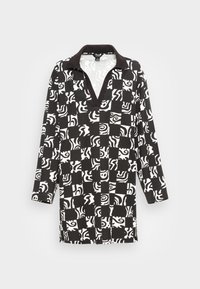 Camisa de manga longa em preto e branco com gola, padrões abstratos únicos em um layout de tabuleiro de xadrez e fendas laterais.